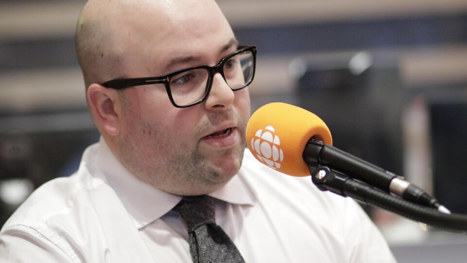 Une homme portant des lunettes parle au micro. 