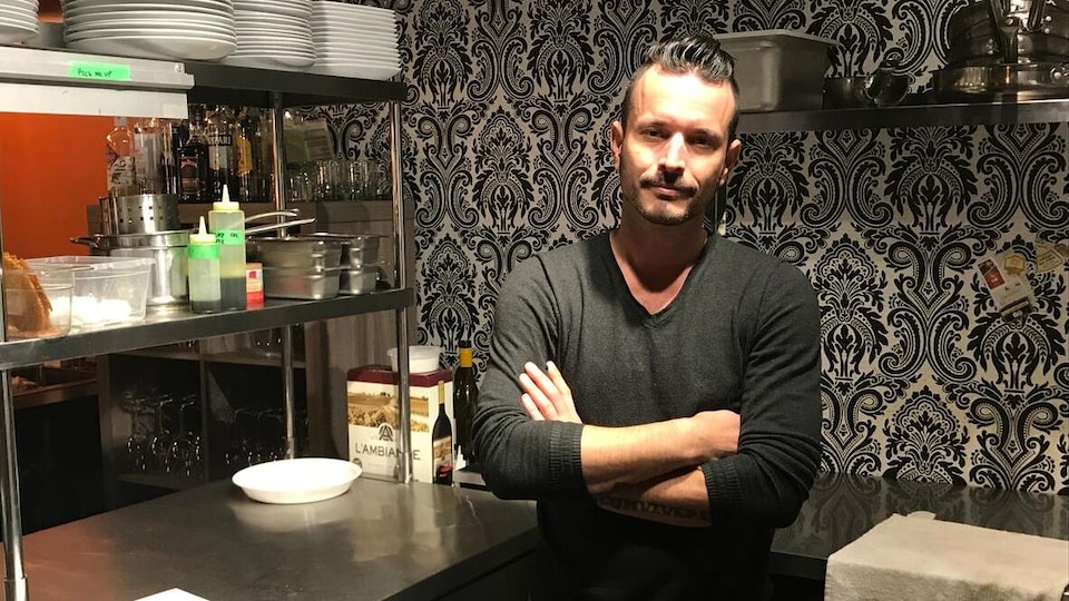 Un homme les bras croisés dans la cuisine d'un restaurant.
