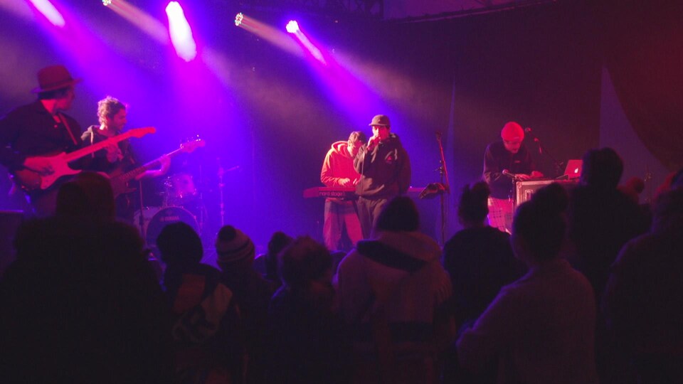 Un groupe de musique se produit sous les projecteurs mauves d'une scène.