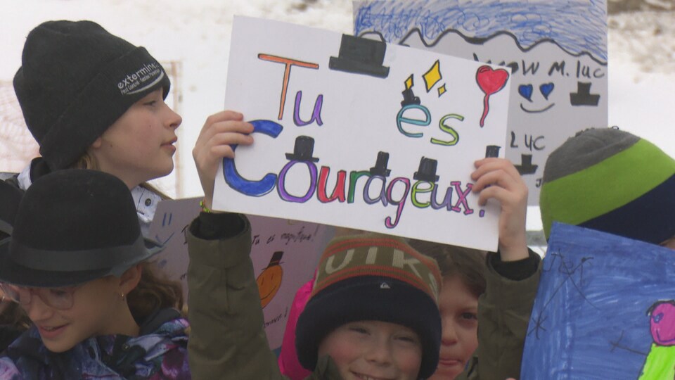 Un enfant souriant tient une pancarte sur laquelle est écrit « tu es courageux ».