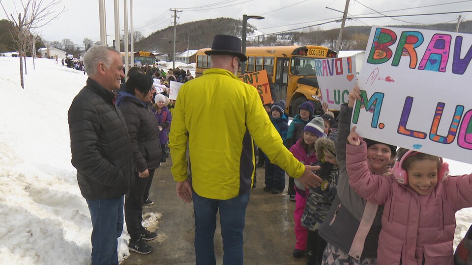 Luc LeBlanc entouré par une haie d'honneur. Des enfants tiennent des pancartes le félicitant. 
