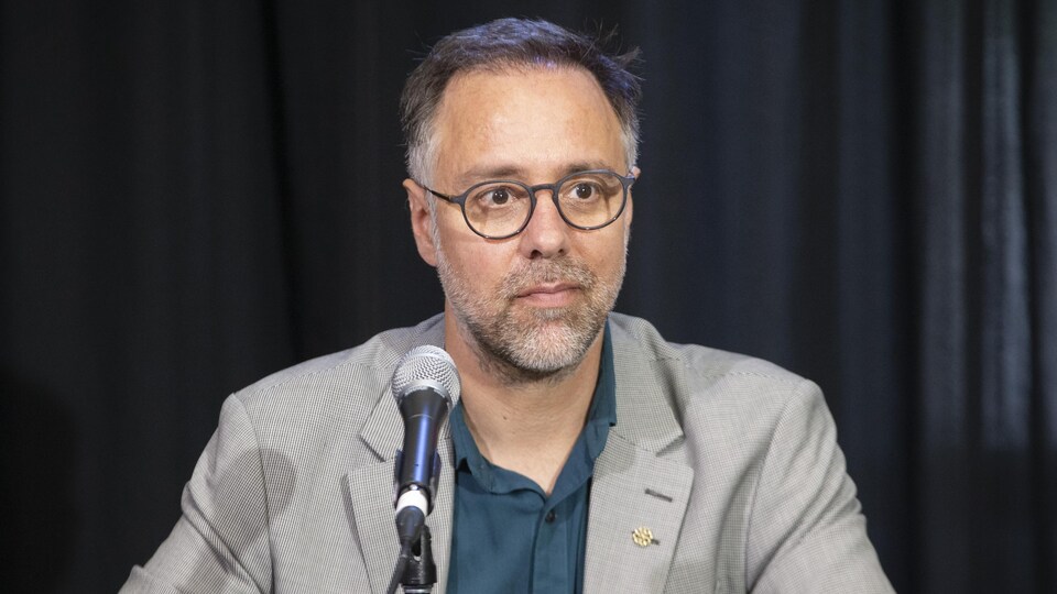 Luc Rabouin assis derrière un micro en conférence de presse.