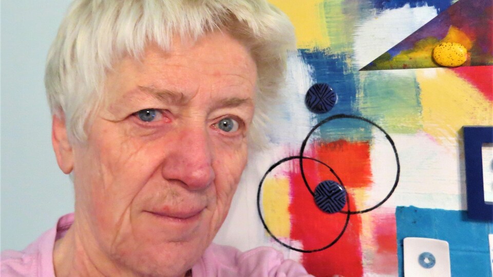 Luce devant un de ses tableaux colorés aux formes géométrique nombreuses.