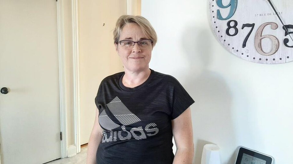 Une femme sourit à la caméra dans son salon.