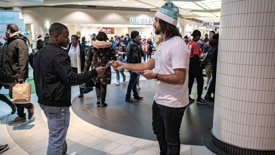 Un jeune homme qui travaille et porte une tuque de NoÃ«l donne un coupon promotionnel Ã  un visiteur du centre Eaton de Toronto.