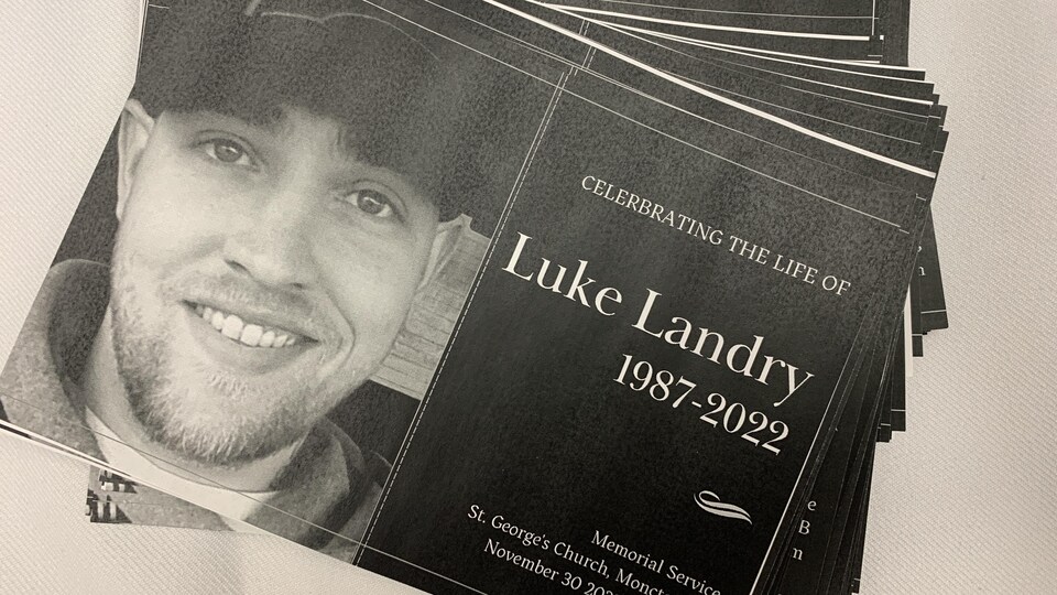 Des dépliants en noir et blanc. On y voit la photo d'un jeune homme souriant et les mots « Luke Landry 1987-2022 ».