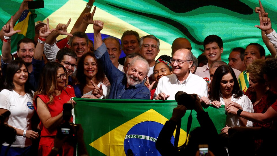 Luiz Inacio Lula da Silva, souriant, lève sa main droite.