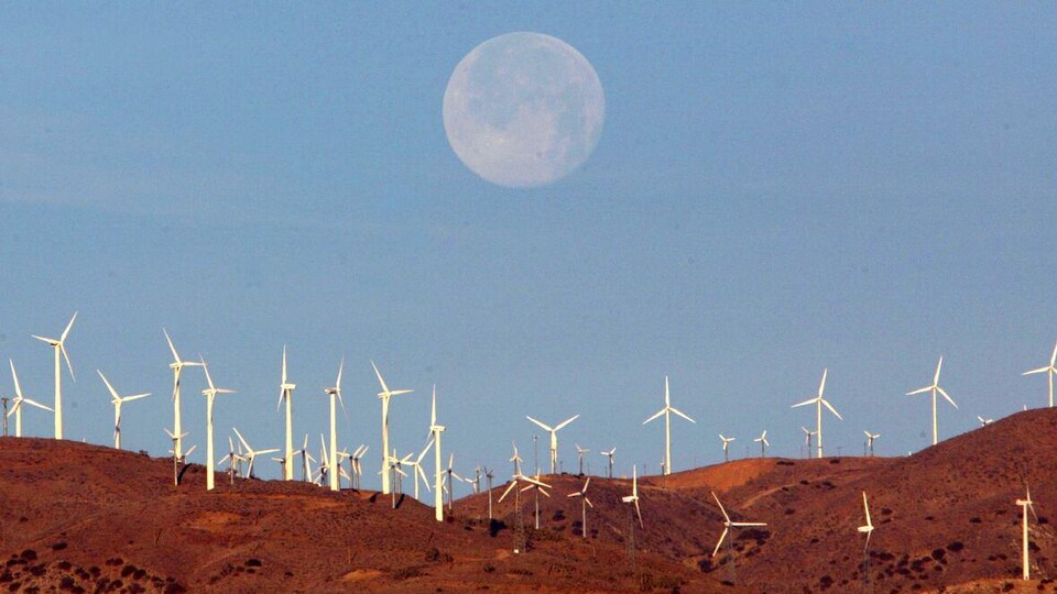 La lune est visible au-dessus d'un parc éolien.