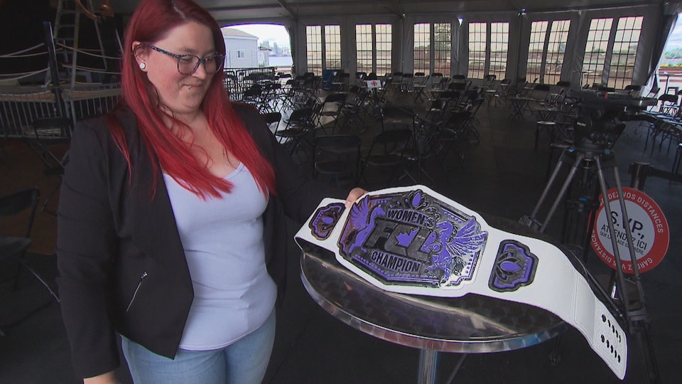 Une femme tient une ceinture de lutte qui est posée sur une table.