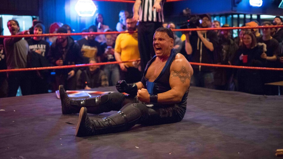 Un lutteur musclé assis dans le ring semble crier.