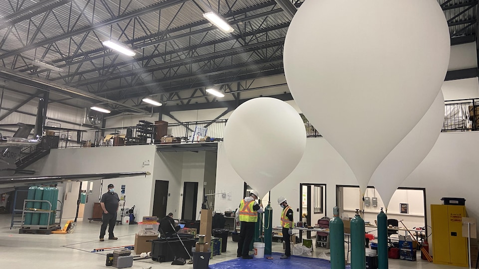 Des ballons blancs énormes sont gonflés dans un hangar d'aéroport.