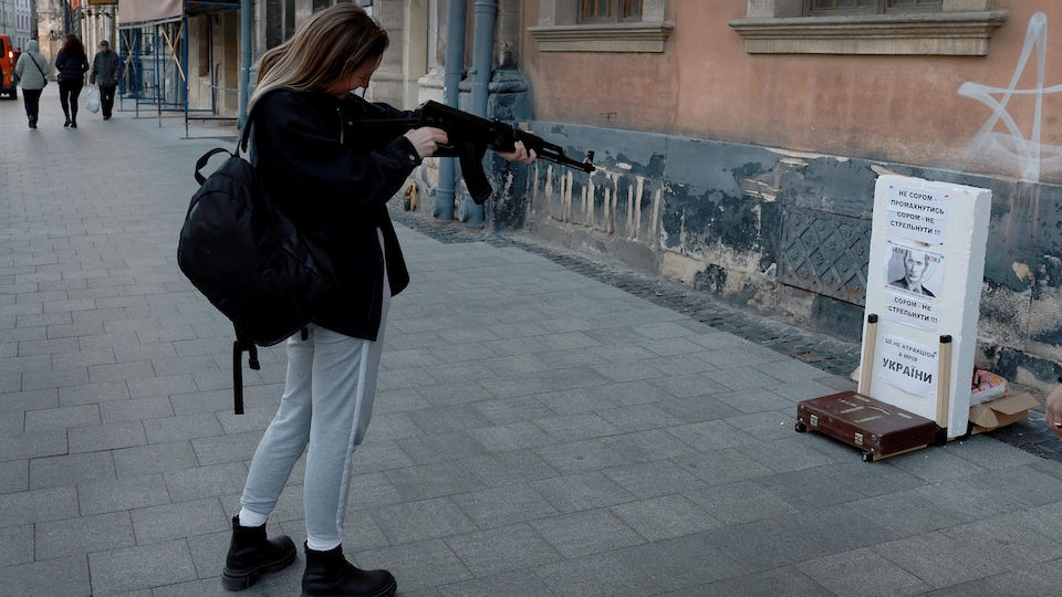 Une femme utilise une arme pour tirer sur une image de Vladimir Poutine placée sur un panneau.