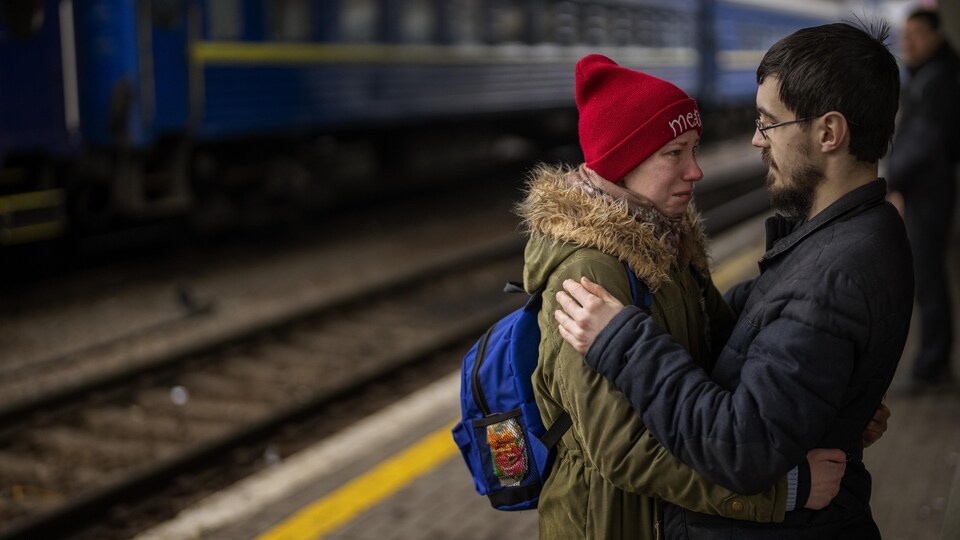 Une femme qui pleure enlace un homme sur le quai d'une station de train.