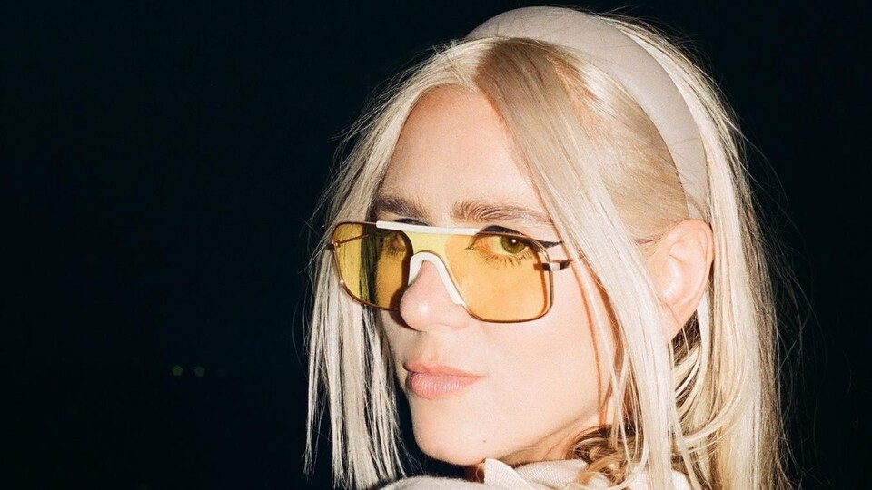 Une femme avec des lunettes teintées jaunes croise les bras.