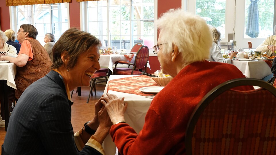 Une dame tient la main d'une résidente âgée dans une cafétéria 