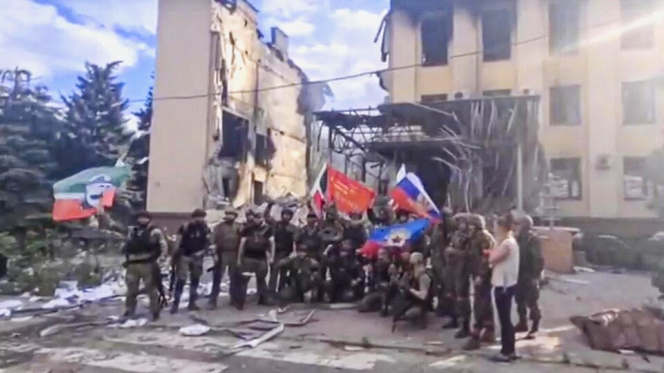Des soldats russes prennent la pose avec des drapeaux devant un immeuble détruit.