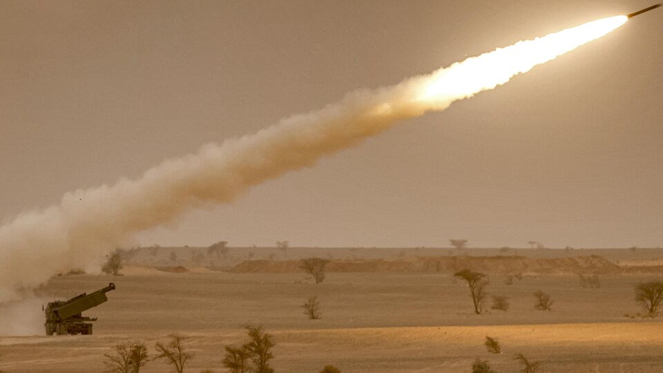 Une roquette, tirée d'un véhicule, laisse une longue flamme dans le sillage de son lancement sur un fond désertique.