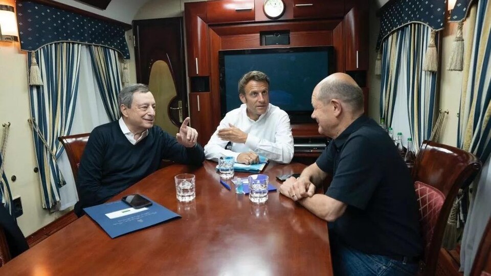 Emmanuel Macron, Olaf Schotlz et Mario Draghi discutent autour d'une table.