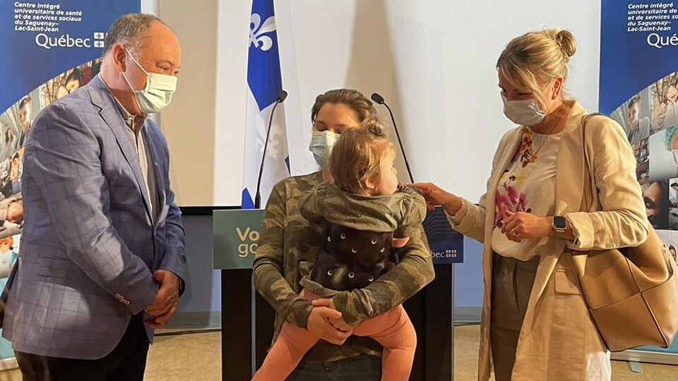 Le ministre Dubé et une femme entourent une femme qui tient une enfant dans ses bras.