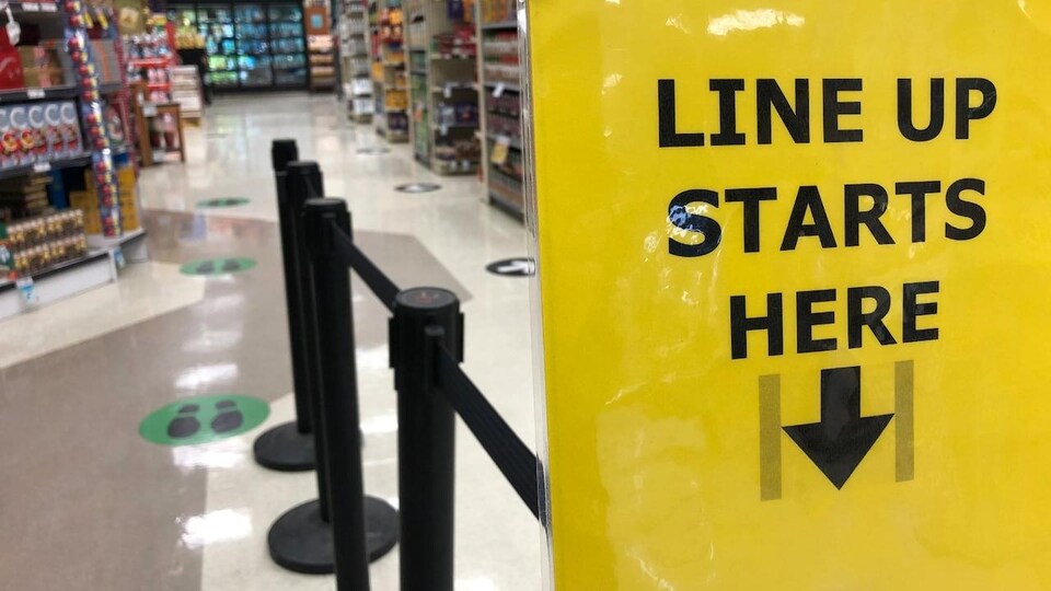 Une affiche jaune montre le début de la file d'attente aux caisses dans une épicerie.