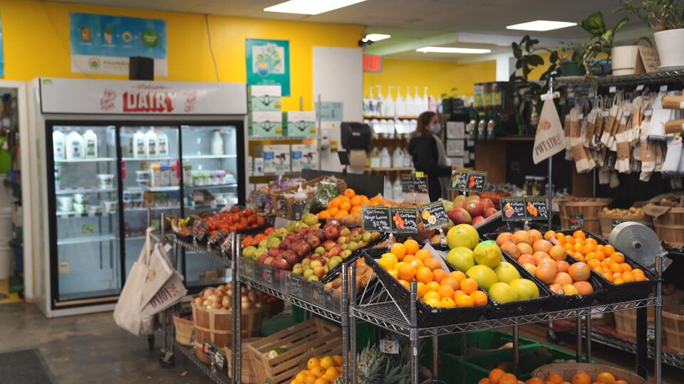 Un étalage de fruits, dont des pommes et des oranges, avec des bouteilles de lait dans un réfrigérateur dans un magasin d'alimentation.