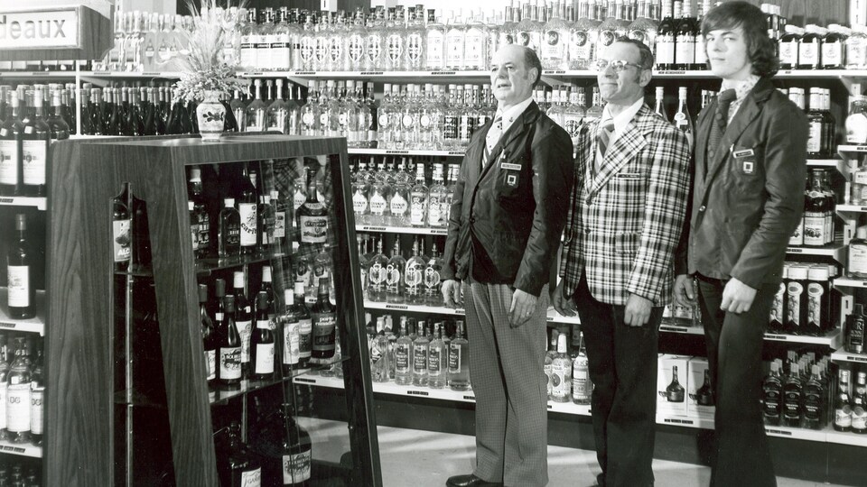 Trois hommes devant des rayons remplis de bouteilles d'alcool