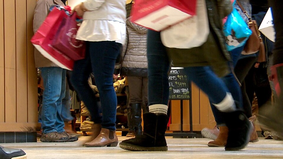 Des personnes marchent dans un centre d'achats avec des sacs dans les mains. 