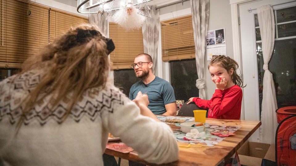 Une famille est réunie autour d'une table en bois pour un repas sous un luminaire décoré pour les fêtes.