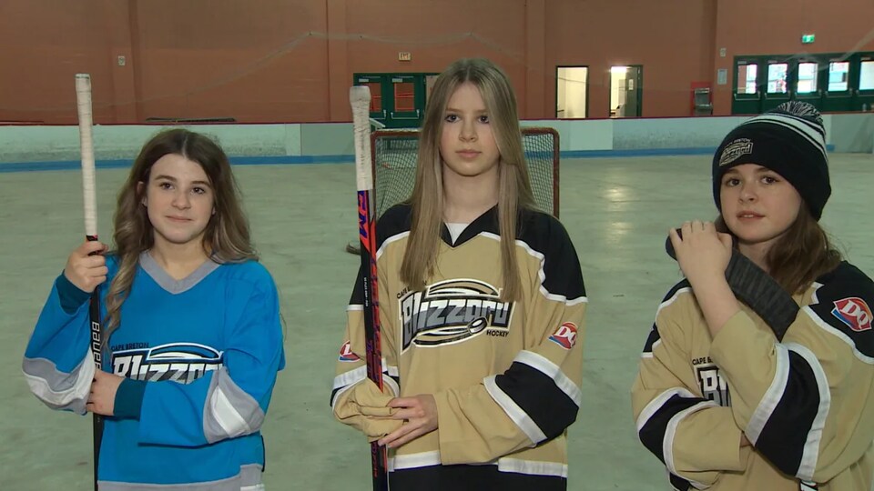 Trois jeunes joueuses tiennent leur bâton de hockey.