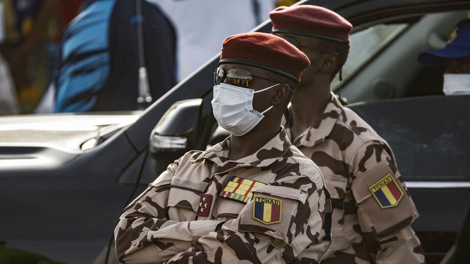 L'homme, portant un uniforme de l'armée, se tient debout les bras croisés.