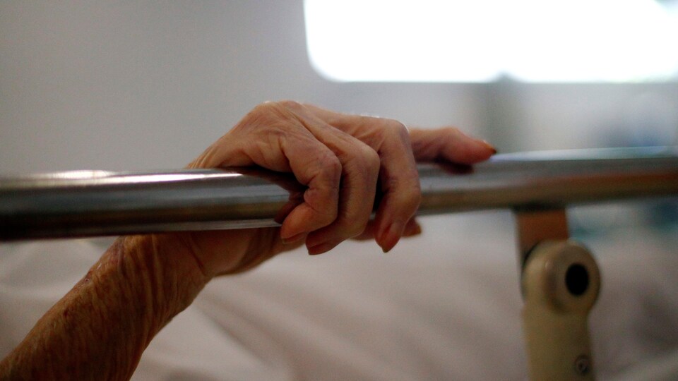 Un patient tient la barre métallique de son lit d'hôpital.