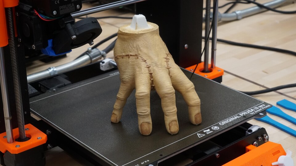 Une main en plastique sur la plaque noire d'une imprimante 3D.