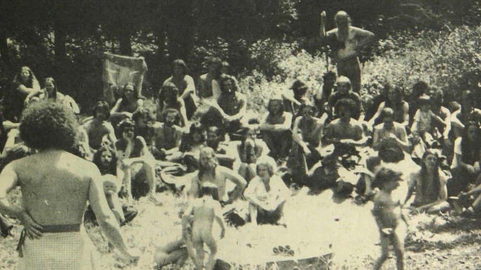 Photo en noir et blanc où on voit des enfants nus et des hippies en plein air.