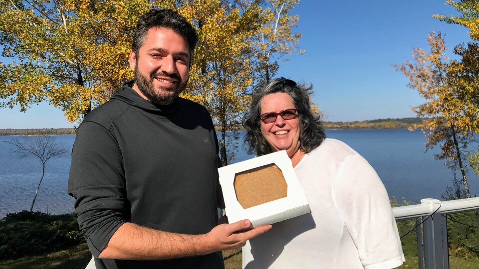 Le maire de Moffet remet une tarte au sucre à Danielle Jodoin alors qu'ils se trouvent dehors au bord de l'eau.