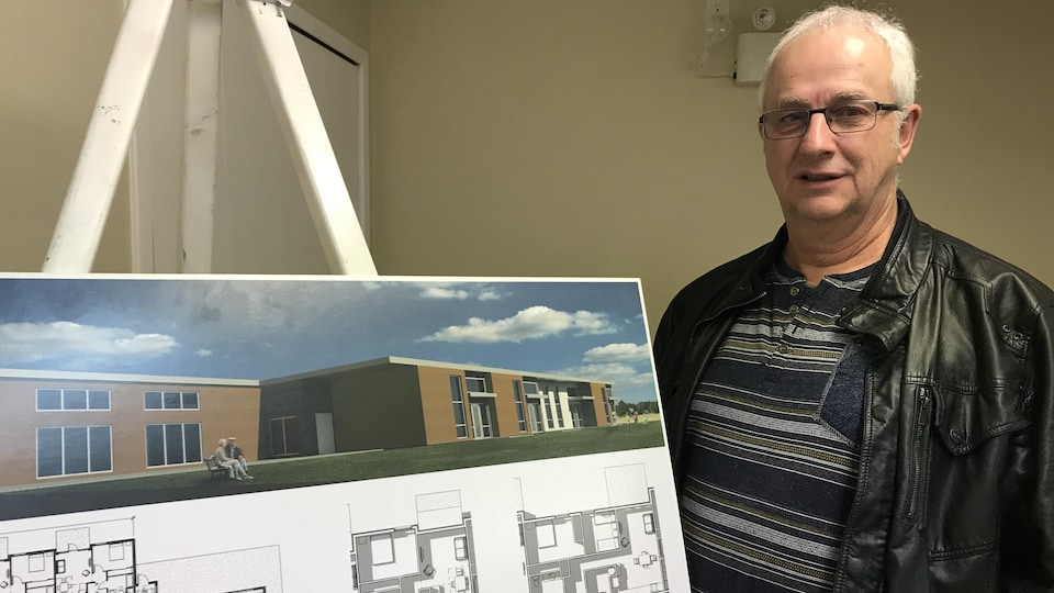 Daniel Barrette pose à côté d'une affiche d'un projet de résidence pour personnes âgées sur lequel in travaille.