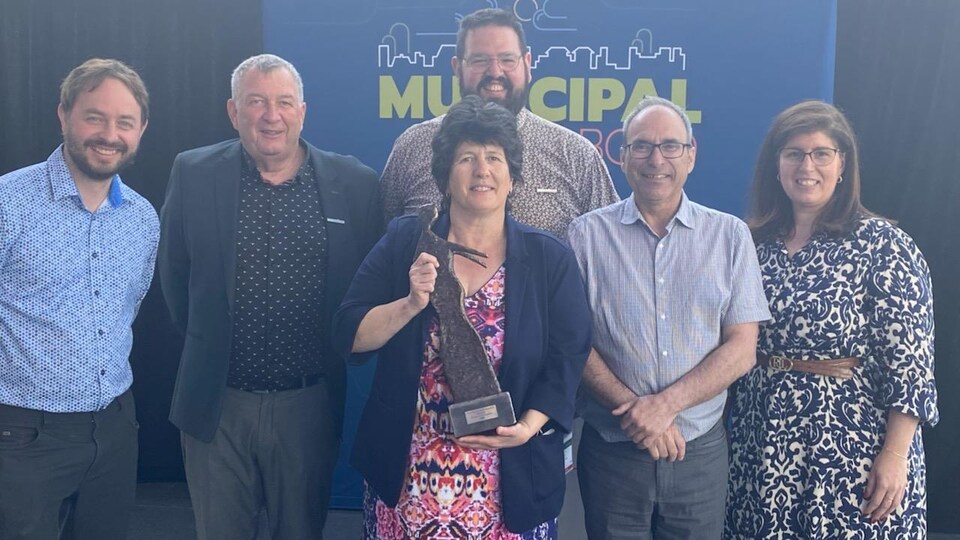 Une femme tient un trophée entourée de personnes.
