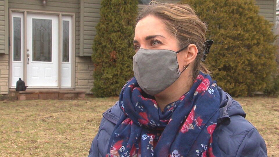 Paula Morin devant sa maison. Elle porte un masque de tissu sur le visage.