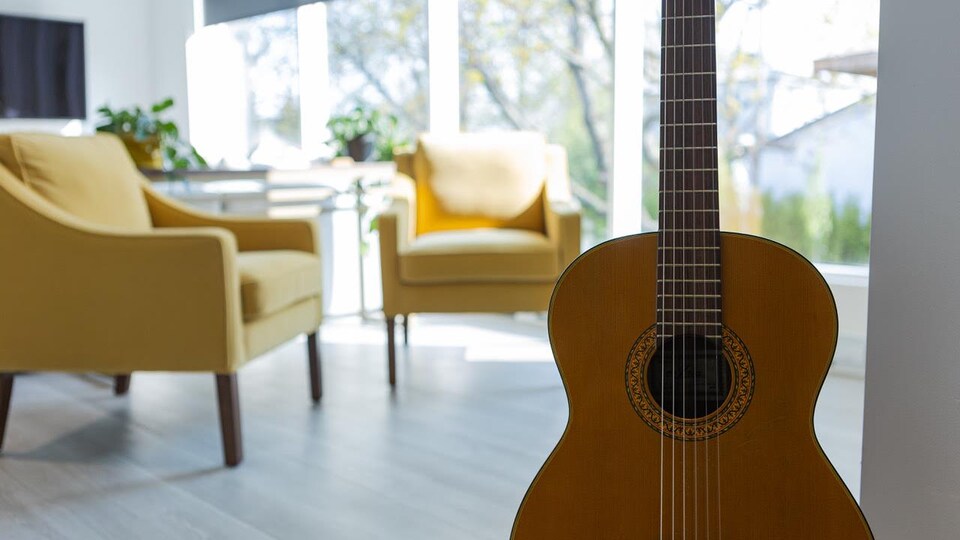 A guitar on a tripod in a living room of the house, in front of the armchairs.