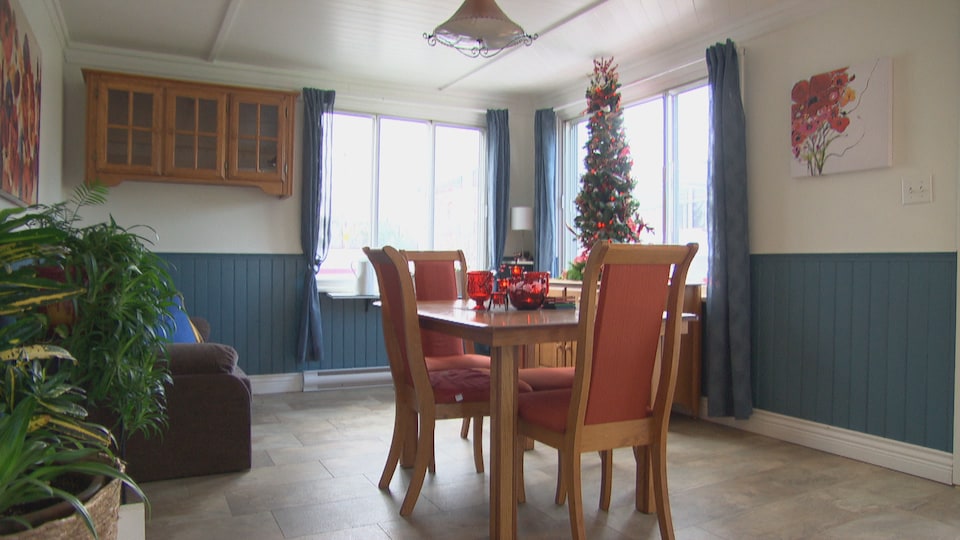 Une salle à manger avec une table, quatre chaises et un sapin de Noël près d'une fenêtre.