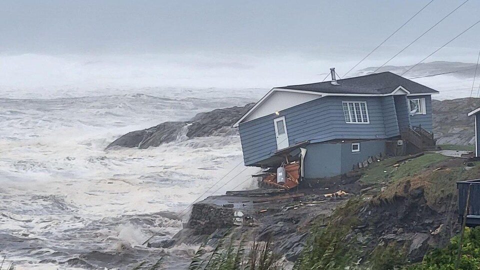 Une maison s'effondre, près d'un littoral lors d'une tempête. 