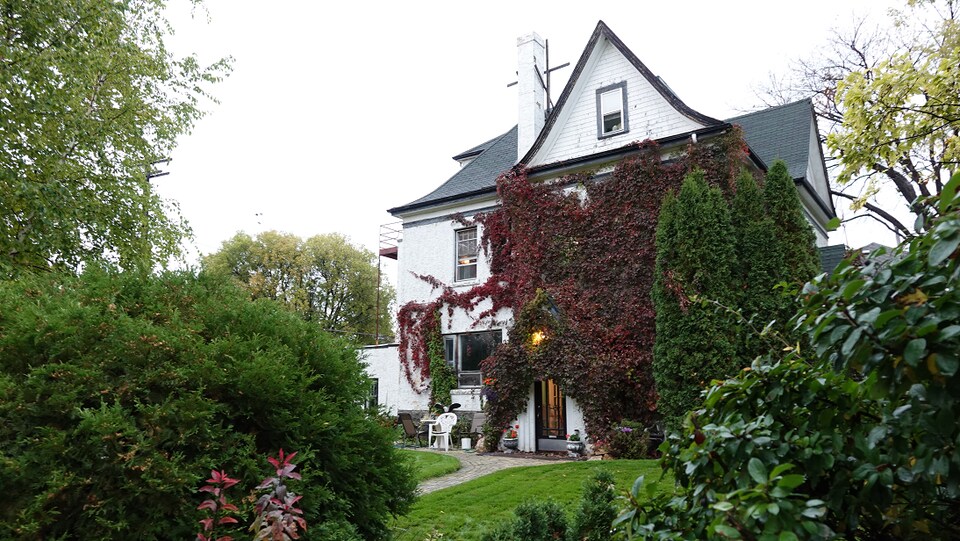 Une maison à trois étages couverte de lierres dans un jardin verdoyant.