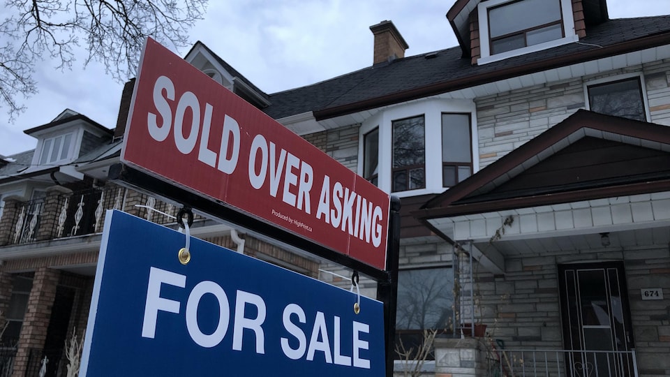 Une affiche de vente immobilière, sur laquelle on peut lire Sold over asking (vendu au-dessus du prix demandé), devant des maisons en rangée.