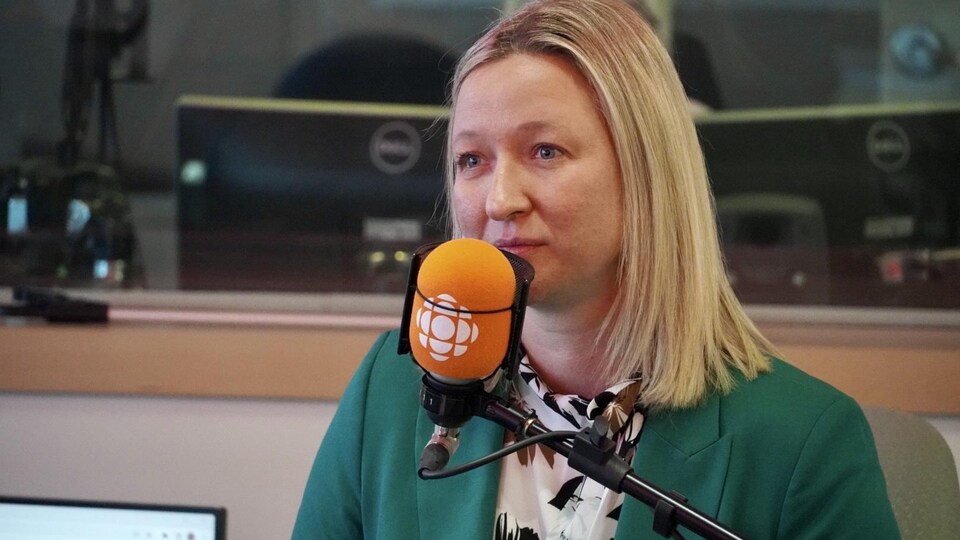 Une femme en veston au micro du studio radio.