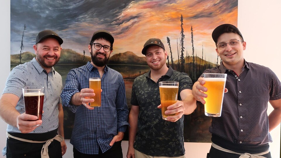 Quatre jeunes hommes tiennent des bières.