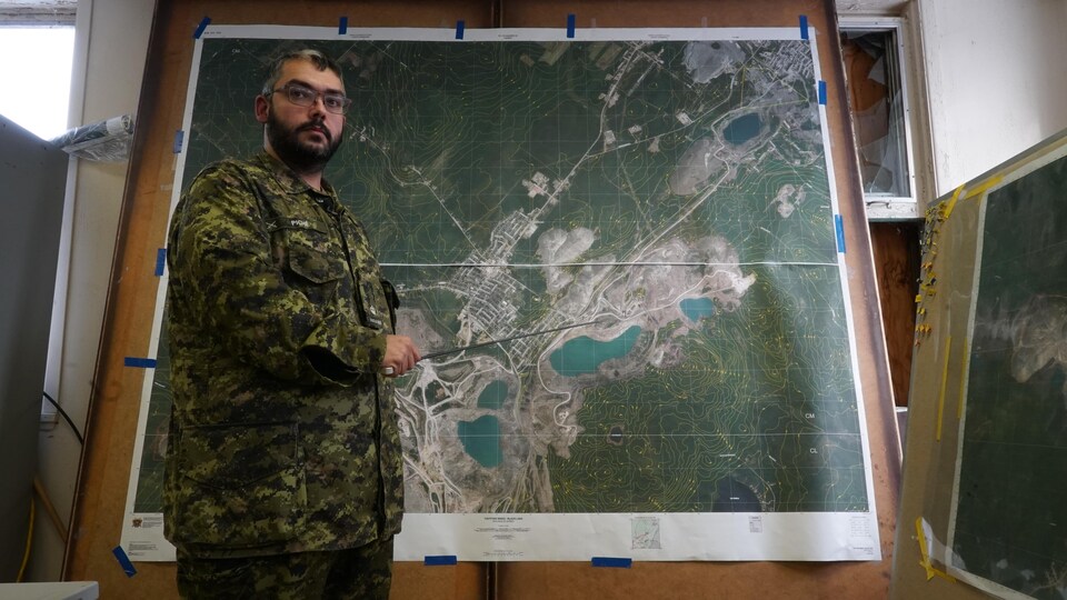 Un militaire se tenant debout devant une carte topographique de la région de Thetford Mines.