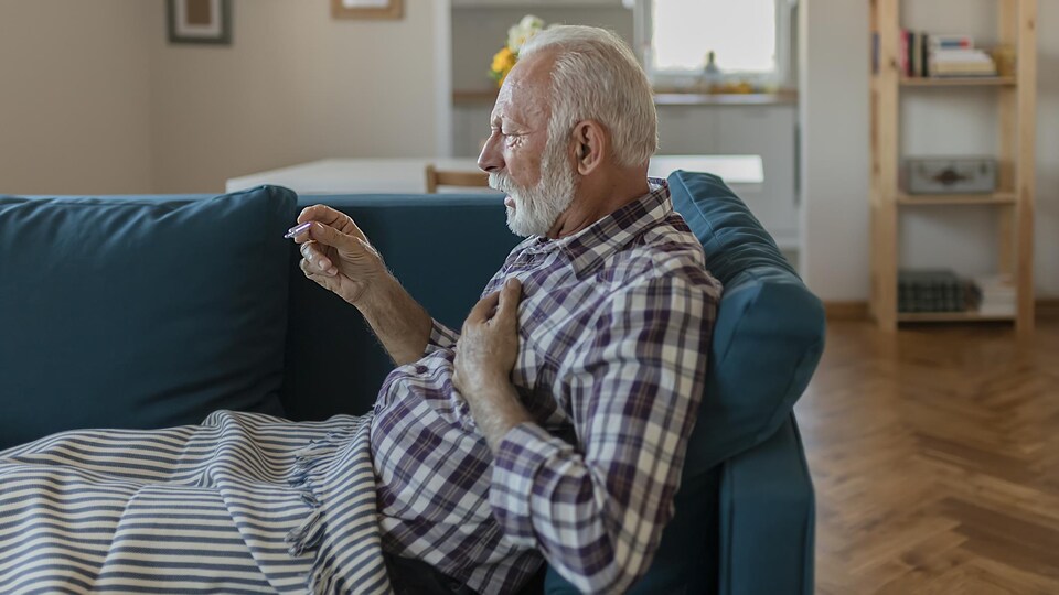 Un vieil homme étendu sur son divan prend sa température.
