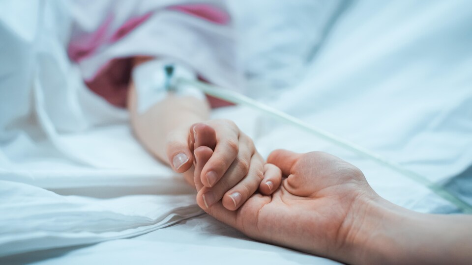 Une personne tient la main d'un malade dans un lit d'hôpital.
