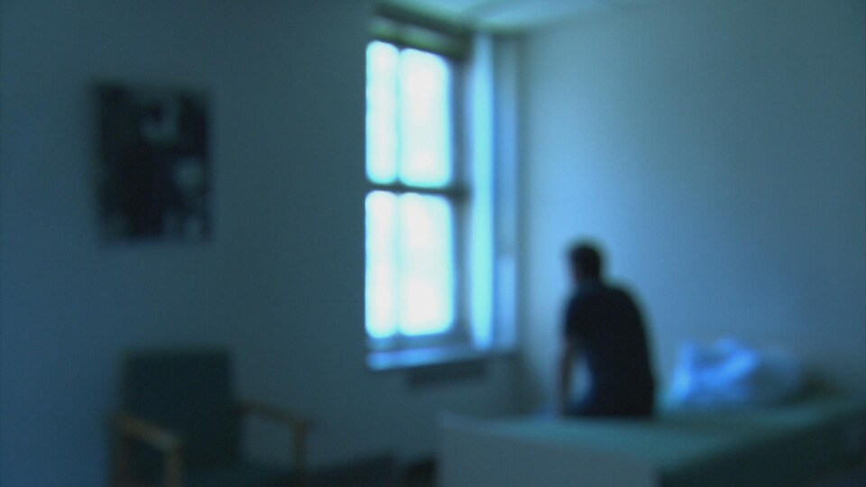 Un patient d'un hôpital psychiatrique assis sur un lit regardant par la fenêtre. 