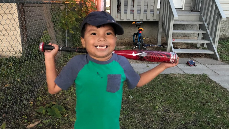 Un jeune garçon tient un bâton de baseball dans son jardin.
