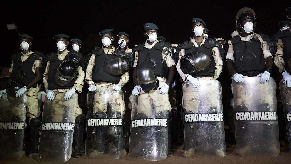 Des soldats en rangs portent masque et gants et tiennent un bouclier.